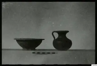 Shallow bowl and single-handled jug standing on a ledge beside a scale bar