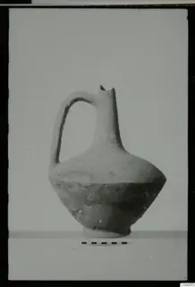 Pottery jug with a strap handle and narrow neck, photographed against a plain background beside a scale bar.