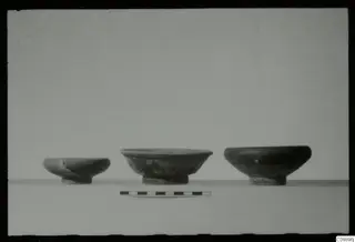 Three bowls with ring feet standing in a row on a pale surface, with a scale bar in front.