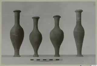 Four narrow-necked pottery jugs of differing heights standing in a row on a plain surface.