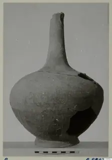 Pottery jar with a tall narrow neck, rounded body and ring foot, photographed against a grey backdrop with a scale bar