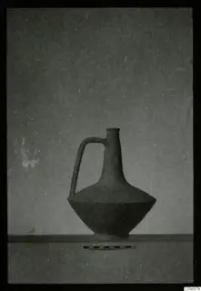 One-handled pottery jug with a narrow neck, standing on a ledge beside a scale bar