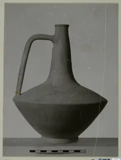 Jug with a tall neck and single loop handle, shown beside a scale bar against a plain grey backdrop