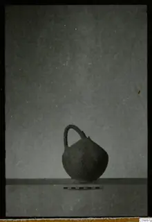 Pottery jug with a single loop handle and a scale bar in front, photographed against a plain grey background.