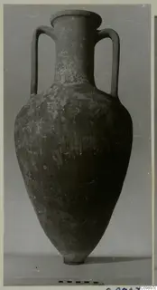 Large two-handled amphora with a narrow neck and pointed base, photographed against a grey backdrop with a scale bar below.
