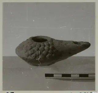 Clay oil lamp with a filling hole on top, a pinched spout to the right and rows of raised knobs on the body, beside a scale bar