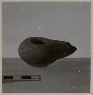 Oil lamp with a rounded body and a pointed nozzle to the right, photographed beside a scale bar
