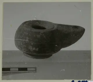 Pottery lamp with a projecting spout and round filling hole, photographed beside a scale bar