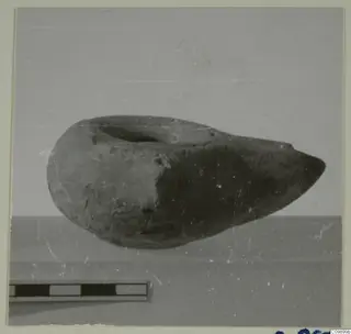 Pottery vessel with a wide round opening and a pointed end, lying on its side beside a scale bar