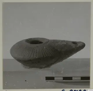 Clay oil lamp with radial grooves on its shoulder and a spout to the right, beside a scale bar