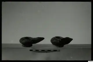 Two oil lamps with pointed nozzles on a pale surface, with a scale bar in front.