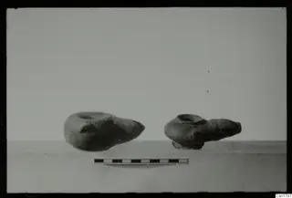 Two pottery oil lamps with pointed nozzles, placed side by side in profile beside a scale bar.