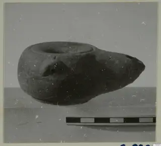 Dark vessel with a wide mouth and tapering spout, photographed on a surface beside a scale bar.