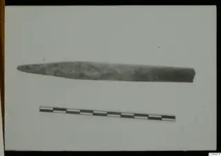 Long, pointed corroded metal object, possibly a tool, with a scale bar below it