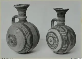 Two White Painted I jugs with round bodies, flared necks and loop handles, decorated with bands and concentric circles.