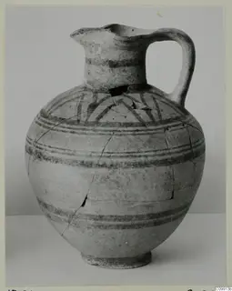 Pottery Bichrome II jug with dark painted bands and arcs on the shoulder, shown against a grey backdrop