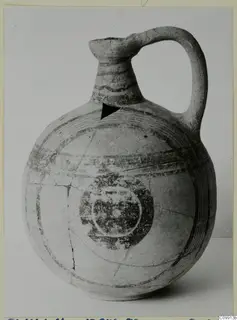 Bichrome V jug with a tall neck, strap handle, painted bands and a dark ring motif on the body