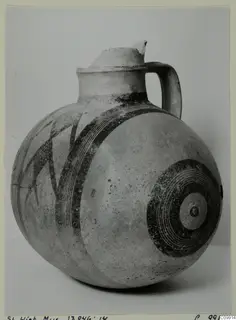 Round-bodied jug with a tall neck, one handle and dark painted bands and concentric circles on a pale surface.