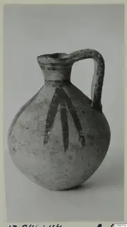Pottery jug with a strap handle and dark painted strokes running down the body