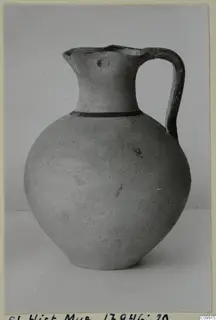 Round-bodied jug with a single dark band at the shoulder and a strap handle, photographed against a plain grey backdrop.