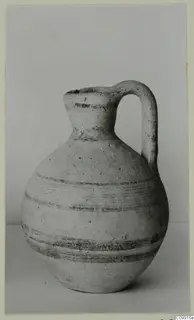 Pottery jug with a single loop handle and dark painted bands around the body, on a plain surface.