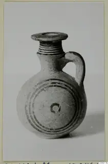 Small round-bodied jug with a ribbed neck, strap handle and dark concentric bands painted on the body