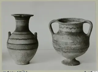 Two painted pottery vessels with handles, one with a flared neck and one standing on a low foot, against a plain background