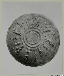 Shallow round bowl seen from above, with concentric raised rings at the centre and raised wavy and hooked motifs around them