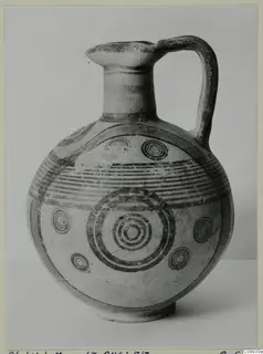 Jug with a strap handle, its round body painted with dark concentric circles and horizontal bands