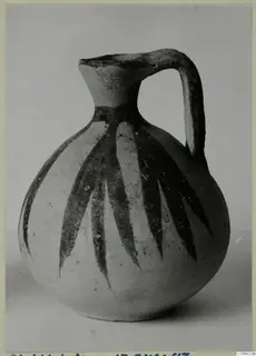 Round-bodied jug with a tall neck, strap handle and dark leaf-like painted strokes on a pale surface.