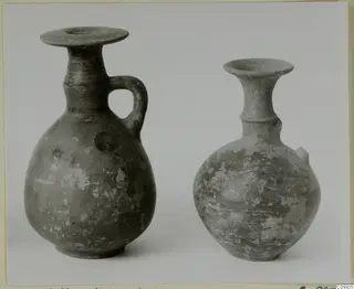 Two pottery vessels side by side, one with a loop handle, on a plain grey background