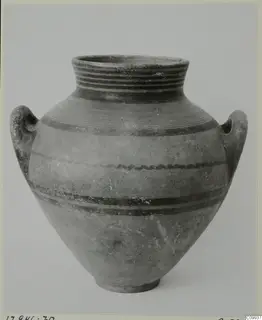 Two-handled jar with dark painted bands and fine rings, photographed against a plain grey background