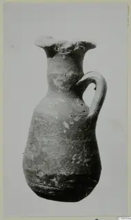 Small pottery jug with a flared mouth and a single strap handle, photographed against a plain background.