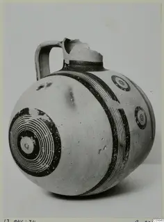 White Painted V jug with a single handle, dark concentric circles and bands on a pale body