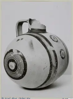 White Painted V jug with a single strap handle, broken neck and rim, and dark bands and concentric circles