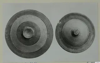 Two round pottery objects seen from above, one larger, both with concentric grooves and a central knob.