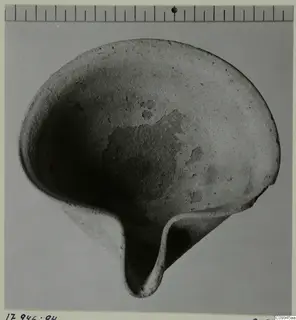 Stone bowl with a pinched lip projecting at one side, photographed from above with a scale bar along the top edge.