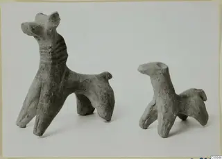 Two small terracotta animal figurines standing side by side on a pale surface