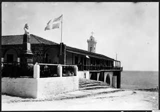 Monastery building in Kyrenia with a flag on a pole, a bell tower with a cross, and a bust on a pedestal