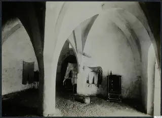 Vaulted interior of a monastery building with a dark cupboard and cloths hung on the walls