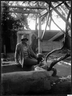 Smiling woman in a hat sits with a dog on a stone ledge in the institute courtyard at Nicosia, under a timber frame.
