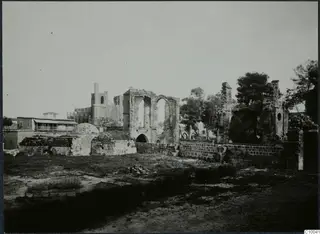Ruined stone buildings with tall arched openings and a slender tower, Famagusta, seen across grass and low walls.