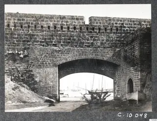 Probably an entrance to the walls of Famagusta: a stone arched gateway opening onto a harbour with moored sailing boats