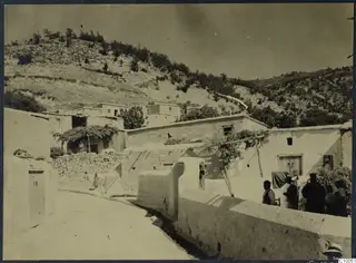Village lane at Machairas, Troodos, with whitewashed houses, a steep wooded hillside and several people beside a wall