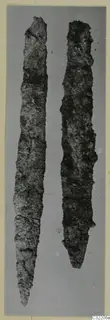 Two long corroded iron tools laid side by side on a plain grey background.