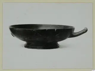 Black-glazed bowl with a single horizontal handle and a low foot, seen from the side.