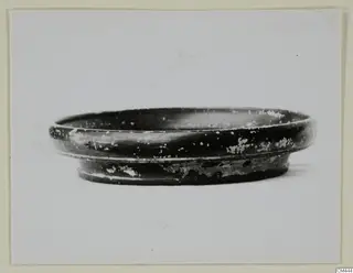 Shallow black-glazed bowl with a low ring foot, seen from the side against a pale background.