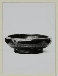 Black-glazed bowl with a low ring foot, photographed in side view against a plain background