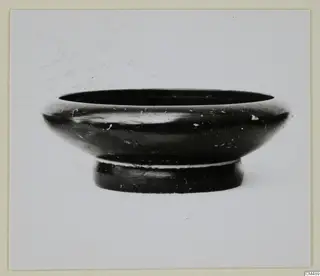 Black-glazed bowl with a wide, rounded rim and a low foot, photographed against a plain background.