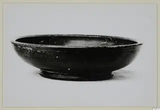 Black-glazed bowl with a ring foot and a chipped rim, photographed against a plain background